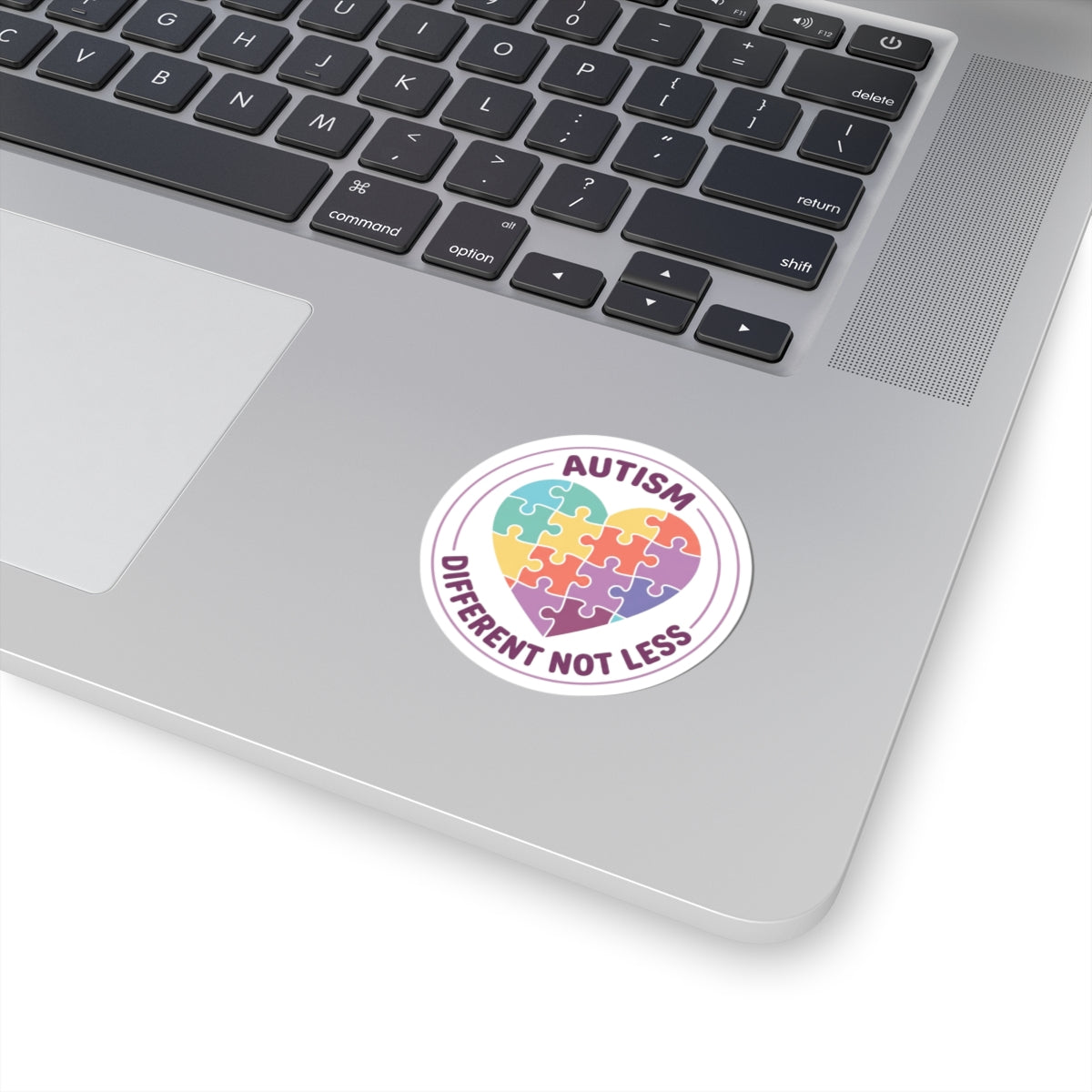 Laptop with a sticker featuring a heart-shaped puzzle piece and text 'Autism Different Not Less' on a white background.